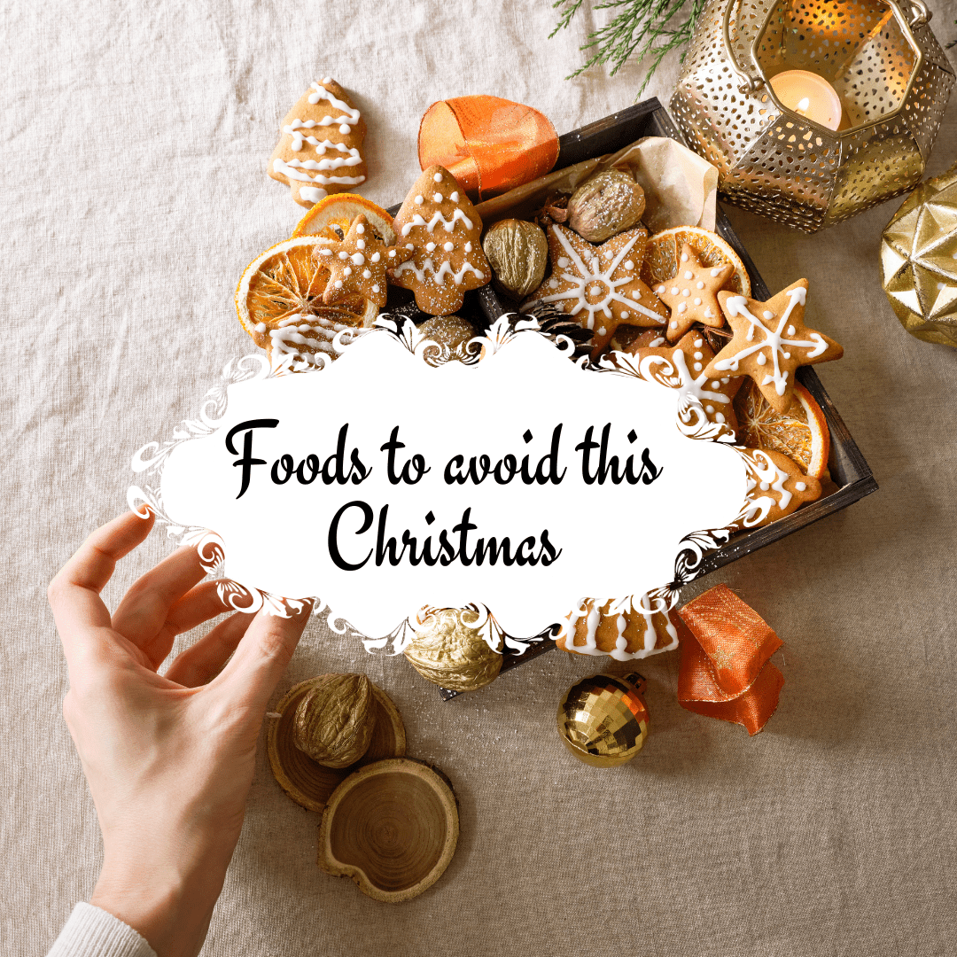 A Christmas-themed image displaying a box of gingerbread cookies, dried orange slices, and nuts on a beige fabric surface, with holiday decorations such as candles and ornaments. A hand reaches for a treat, while a decorative text overlay reads, "Foods to avoid this Christmas."
